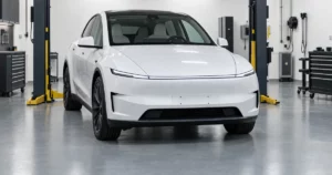 A white Tesla Model Y in a service bay with lifts and tool cabinets